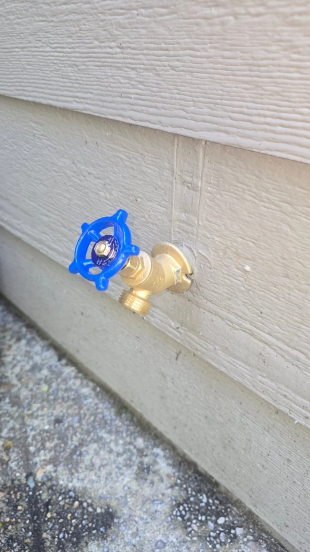 A brass outdoor hose bib spigot with a blue handle installed on exterior siding in Rainier, OR.