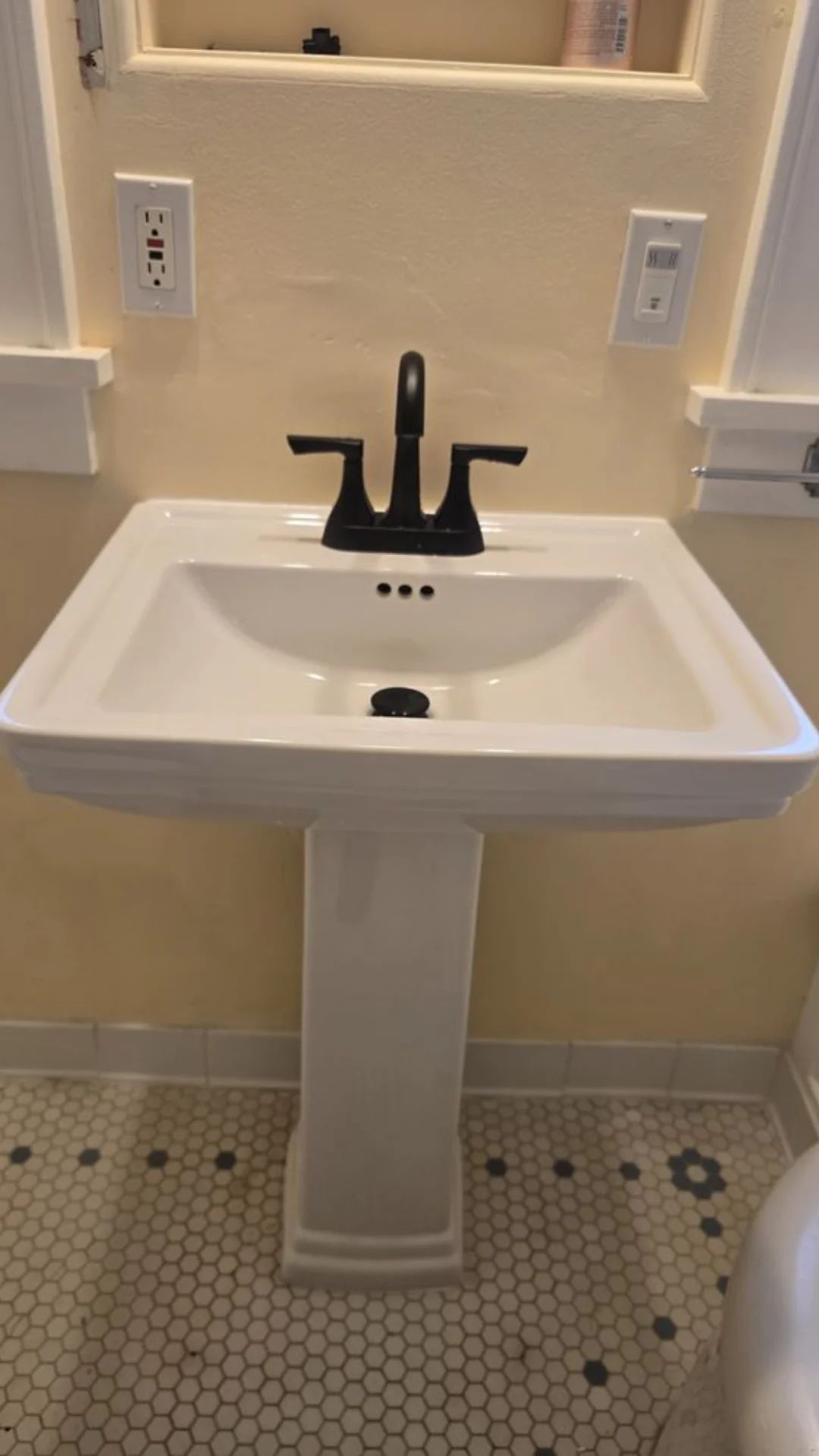 A white porcelain pedestal sink fitted with a matte black faucet on tile flooring in Hillsboro.